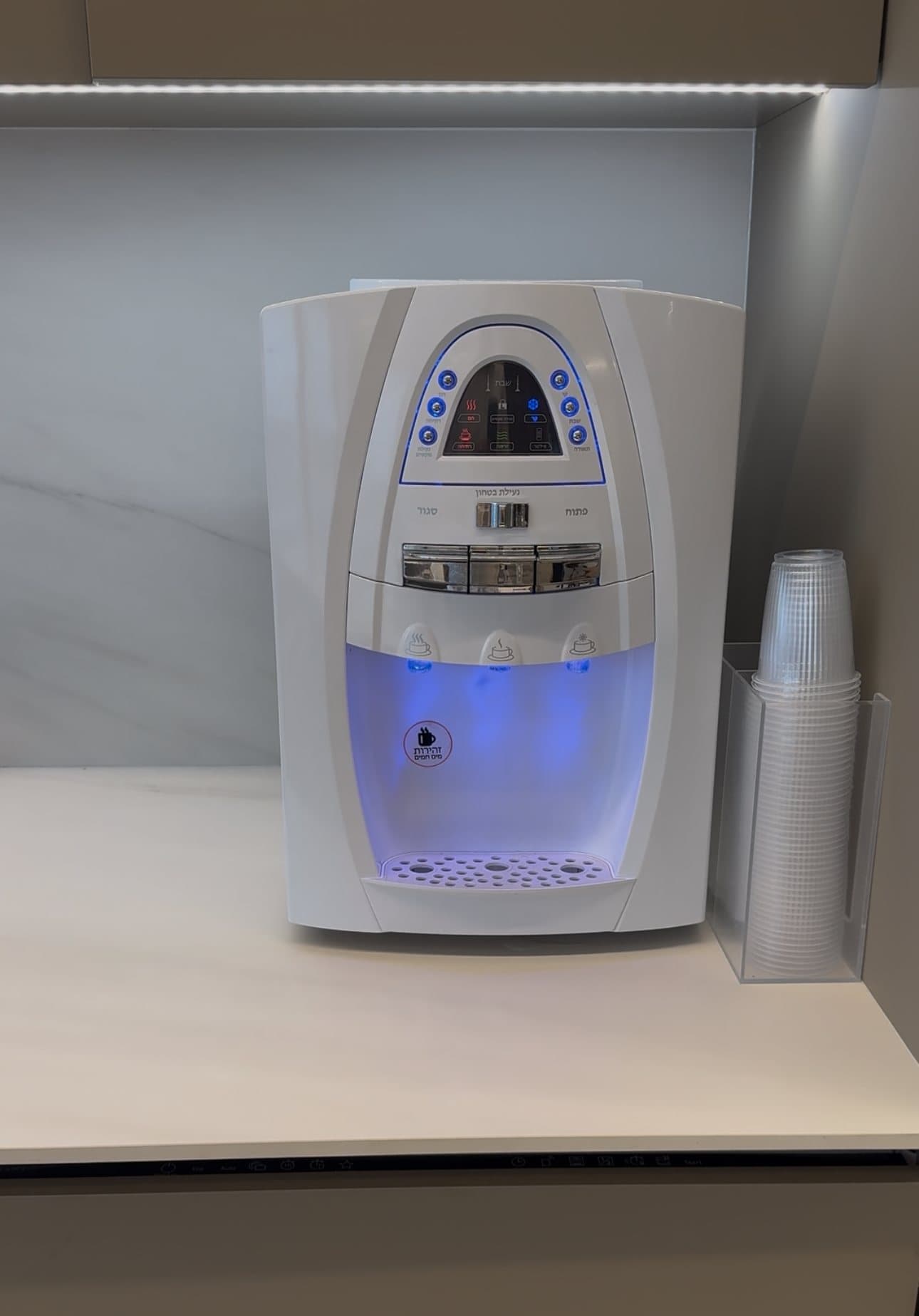 Fontaine à eau Bar Maïme blanche installée sur un plan de travail en marbre, à côté d’un distributeur de gobelets